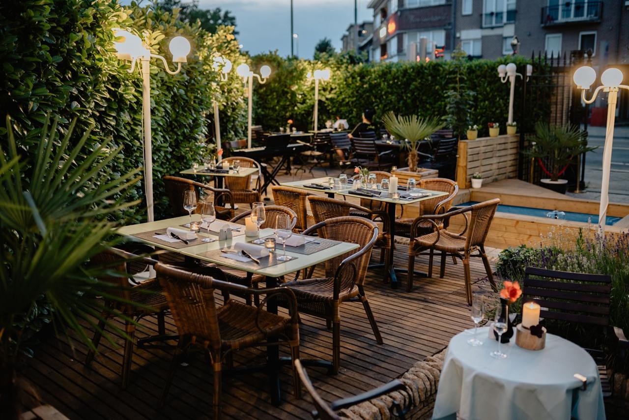 Terrasse de restaurant éclairée en soirée, tables dressées et fauteuils en rotin